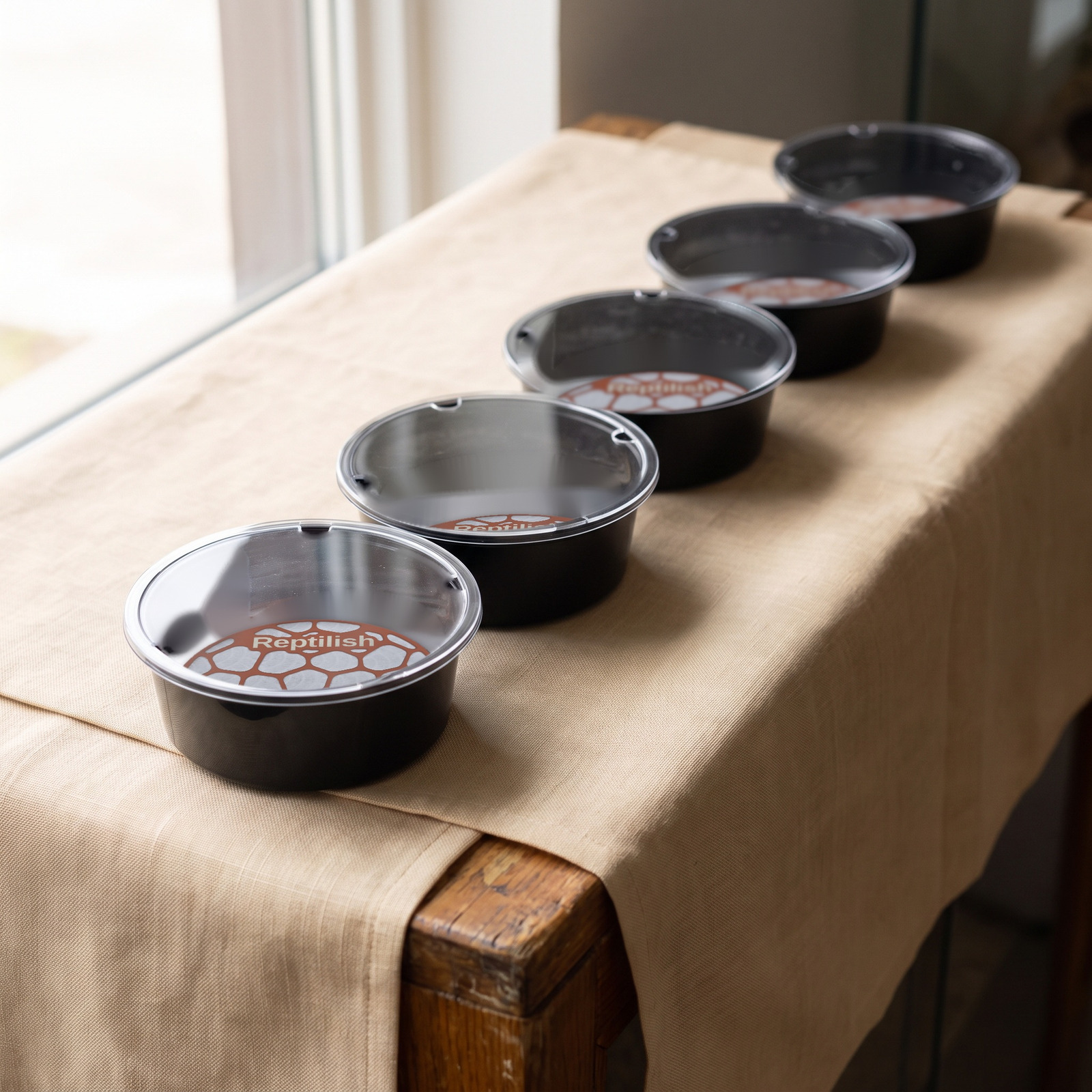 Okrągłe pojemniki z pokrywami akrylowymi na ladzie w sklepie, z przodu płytki Pebble Plate w kolorze Terracotta